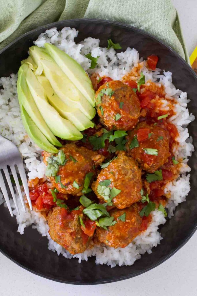 Easy tex mex meatballs recipe served over rice and topped with cilantro in a black plate.