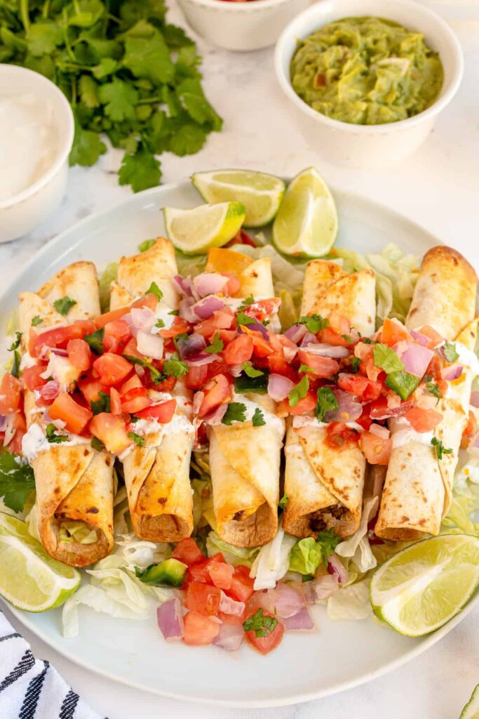 crispy beef taquitos served on a white plate with fresh salsa and sliced lemons