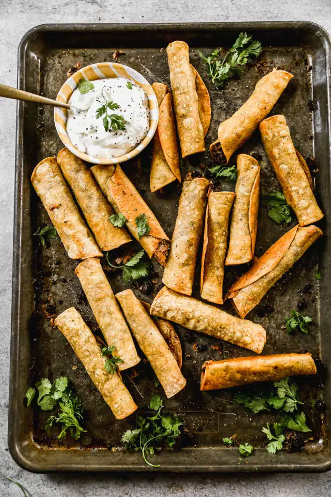 crispy beef taquitos served with sour cream dip in a baking tray