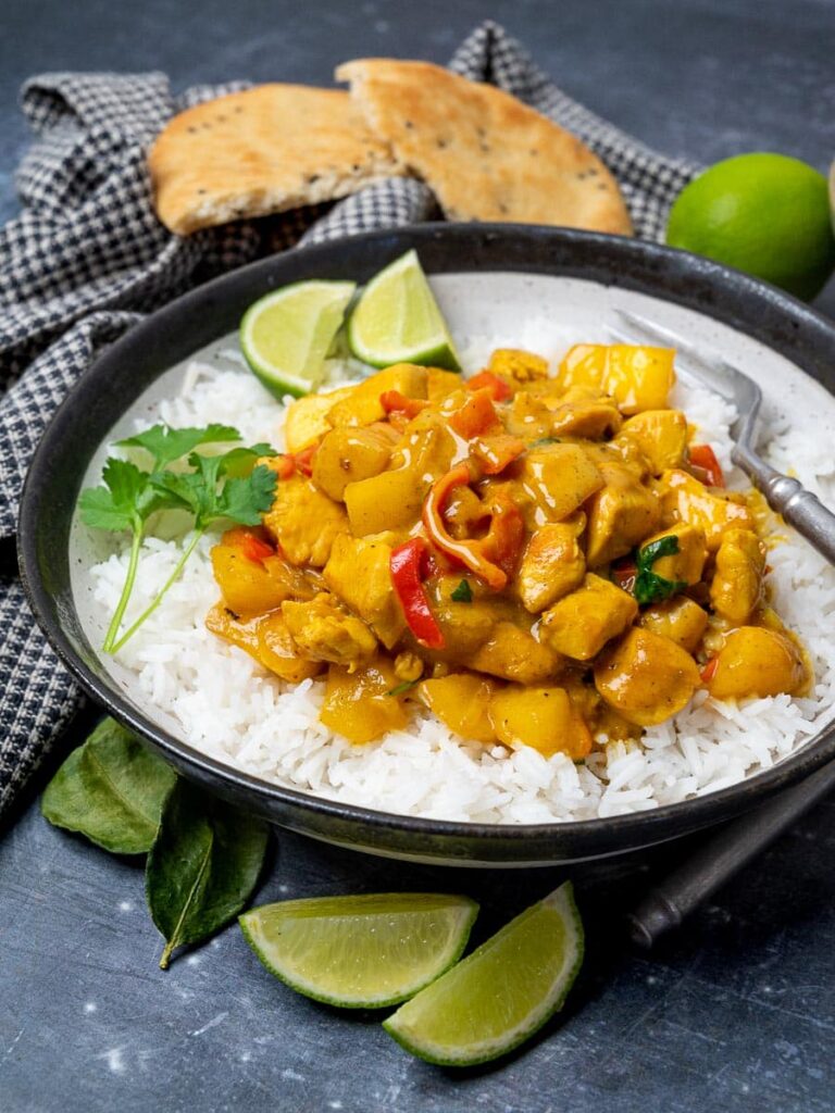 Spicy mango chicken curry with rice in a bowl on a table and fresh slices of lime.