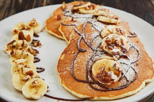 Easy Vegan Banana pancakes with with fresh banana slices, chocolate sauce and topped with walnuts on a white plate