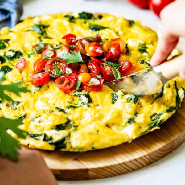 homemade spinach and vegetables frittata topped with cherry tomatoes on a round wooden chopping board